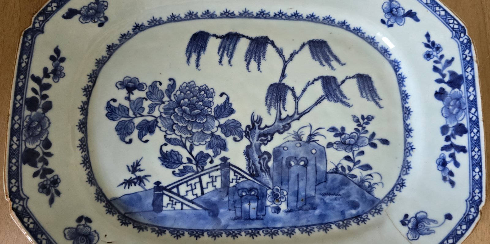 A blue and white plate featuring a detailed garden scene, showcasing flowers and greenery in a serene design.